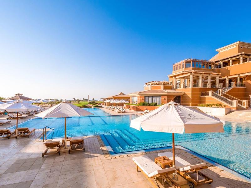 Luxury resort with large pool, sun umbrellas, and lounge chairs under clear blue sky.