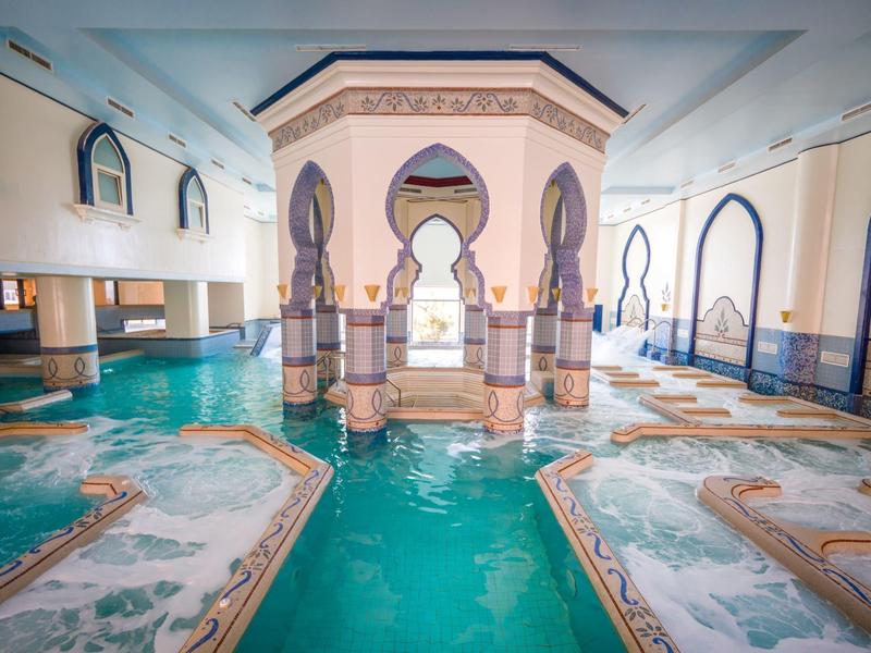 Luxurious indoor pool with ornate columns and mosaic tiles in a hotel.