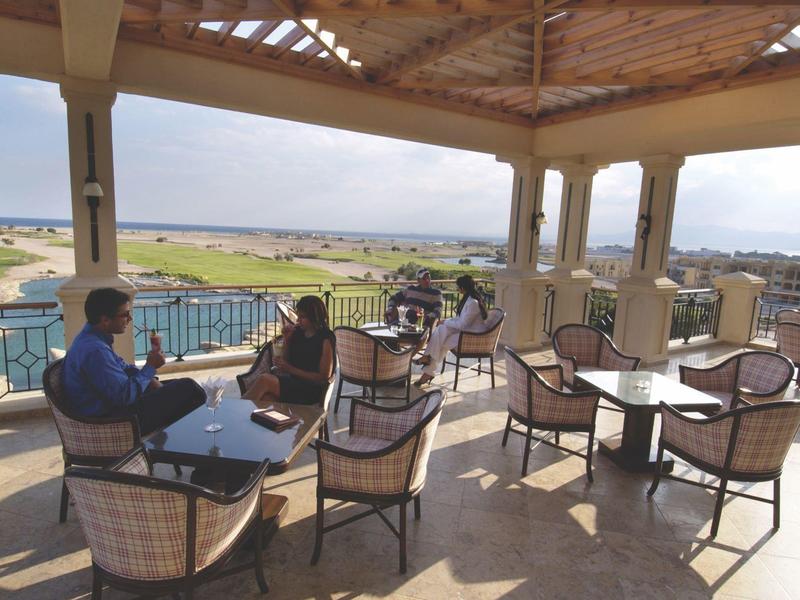 Open terrace with tables and chairs, guests enjoying view of pool and landscape.
