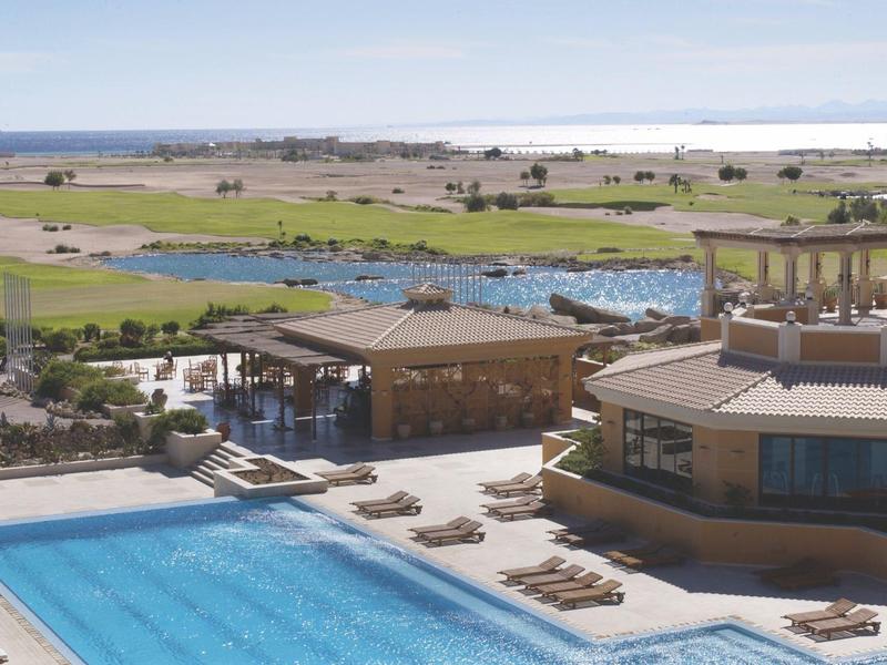 Modern hotel pool with sun loungers overlooking golf course and sea.