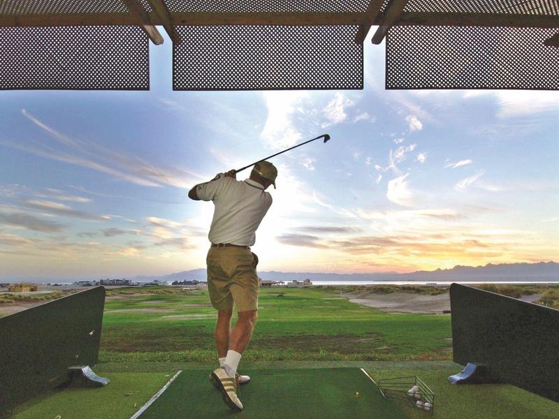 Person hitting a golf ball on a driving range at sunset.