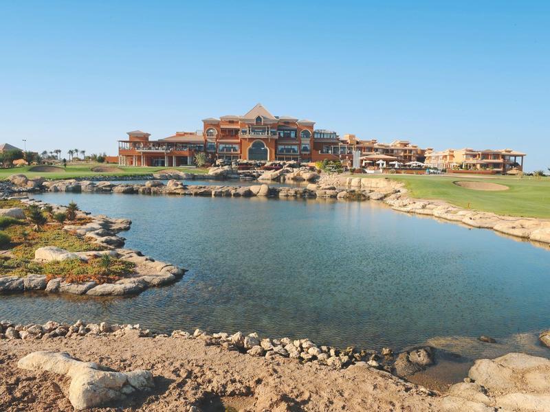 Luxury hotel in front of a pond with manicured lawns under clear skies.