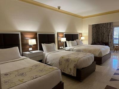 Drei Betten mit weißen Bettwäsche und Nachttischen in einem modernen Hotelzimmer mit dunklen Vorhängen.