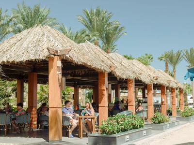 Aree salotto coperte con tetti di paglia e travi in legno in hotel tropicale accanto a una piscina.