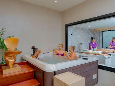 Tre donne si rilassano in una jacuzzi di una spa moderna con uno specchio grande e decorazioni.