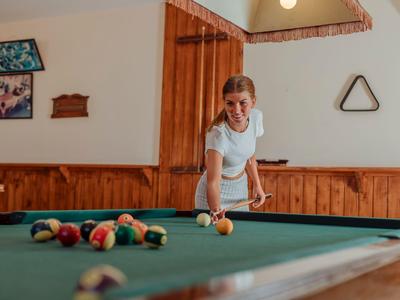 Donna che gioca a biliardo in una stanza rustica con rivestimenti in legno.