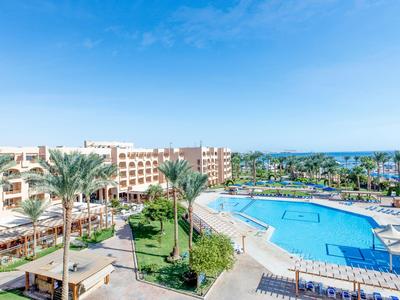 Grande complesso alberghiero con piscina all'aperto, ombrelloni e palme sotto un cielo sereno.