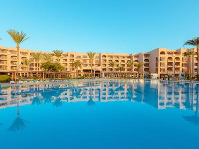 Hotel con grande piscina e palme sotto un cielo azzurro e limpido.