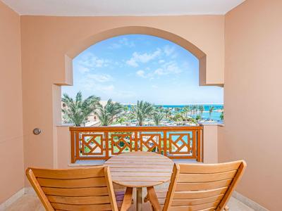Balcone con due sedie di legno e un tavolo con vista su palme, spiaggia e mare