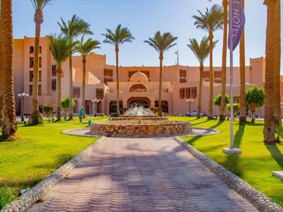 Hotel with fountain, palm trees, and paved walkway in sunny weather