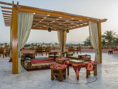 Offener Holzpavillon mit Vorhängen, Teppichen und niedrigen Sitzmöbeln auf einer Terrasse.