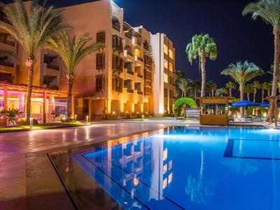Hotel with illuminated outdoor pool at night, surrounded by palm trees and a relaxed atmosphere.