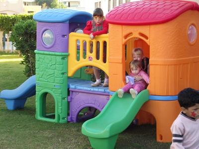 Bunte Spielburg mit Rutsche, Kindern beim Spielen, Gras und Sträuchern im Hintergrund.