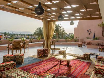 Open terrace with colorful rugs, cushioned floor seating, and tables under a wooden pergola.