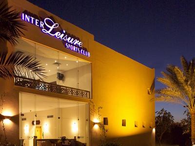 Exterior view of a yellow-lit hotel at night with palm trees in the foreground.