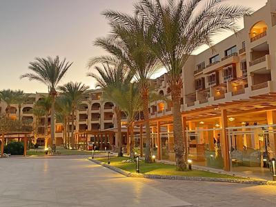 Hotel building with balconies and palm trees at sunset, softly lit.