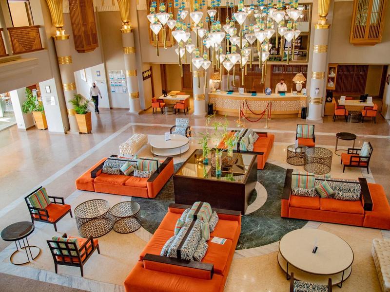 Großer, heller Aufenthaltsraum mit orangenen Sofas, runden Tischen und vielen Lampen an der Decke.