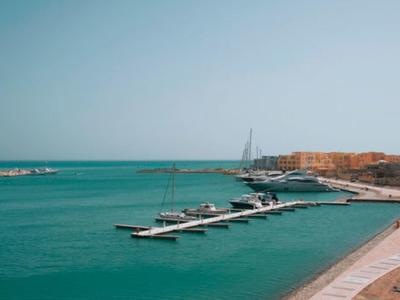Mer bleue calme avec yachts et bateaux amarrés près d'une côte sous un ciel clair.