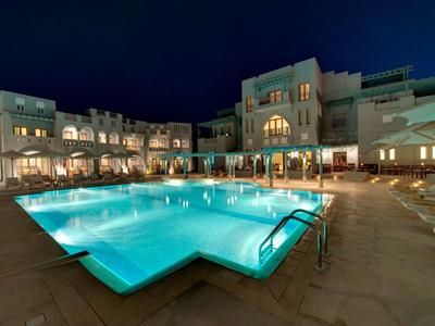 Vue nocturne d'une piscine d'hôtel éclairée avec transats et parasols autour.
