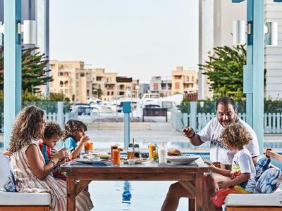 Famille profitant d'un repas en plein air avec vue sur le port en arrière-plan.