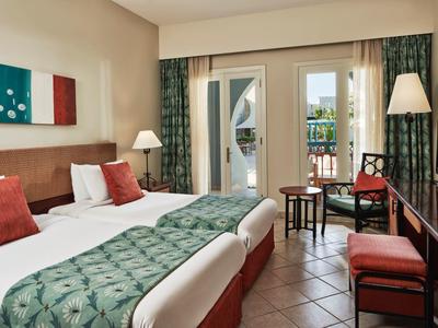 Chambre d'hôtel avec deux lits simples, décoration verte et rouge, et balcon avec mobilier extérieur.