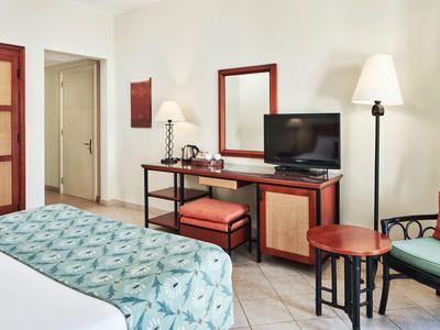 Modern eingerichtetes Hotelzimmer mit Bett, Fernseher, Stühlen und warmem Licht.