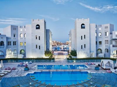 Hotel s bazénem a bílou hranatou architekturou při západu slunce.
