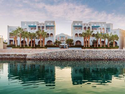 Moderní hotelový komplex s bílými budovami a palmami u vody.