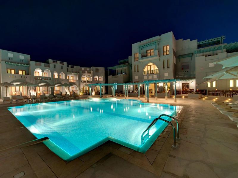 Vue nocturne d'une piscine d'hôtel éclairée avec transats et parasols autour.