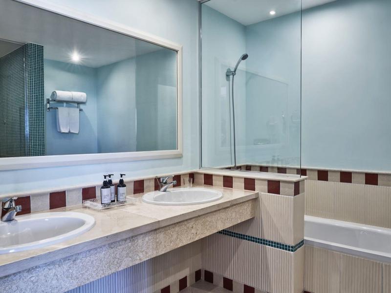 Salle de bain moderne avec deux lavabos, grand miroir et baignoire avec paroi de douche.