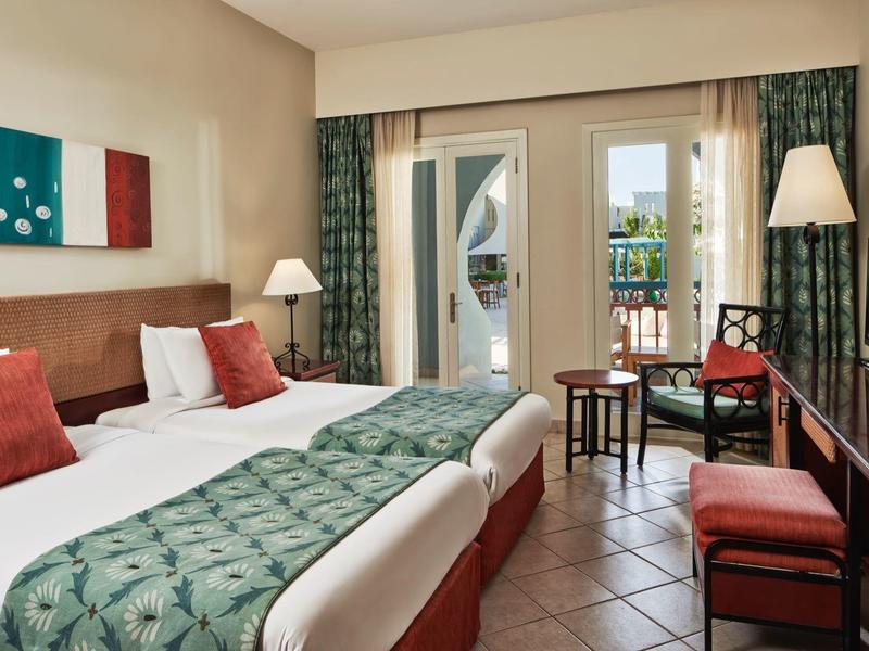 Chambre d'hôtel avec deux lits simples, décoration verte et rouge, et balcon avec mobilier extérieur.