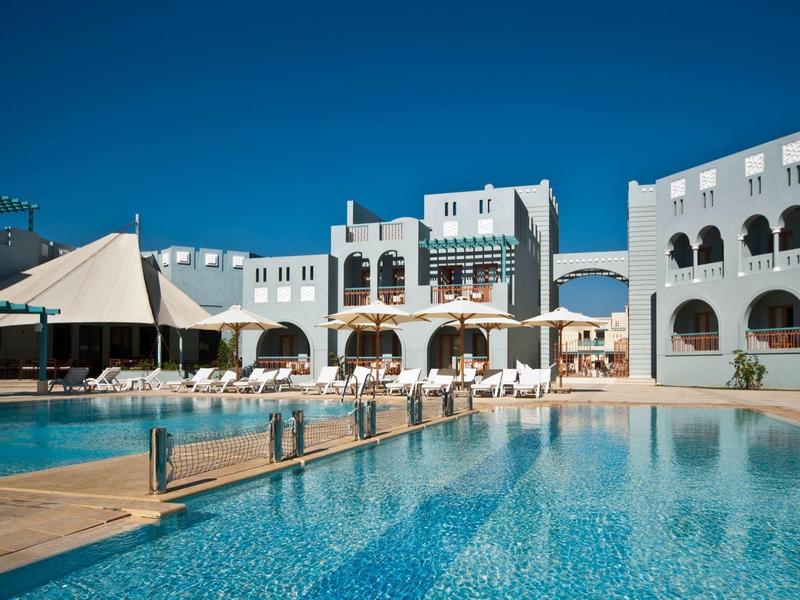 Grand espace piscine d'hôtel avec transats, parasols et ciel bleu clair.