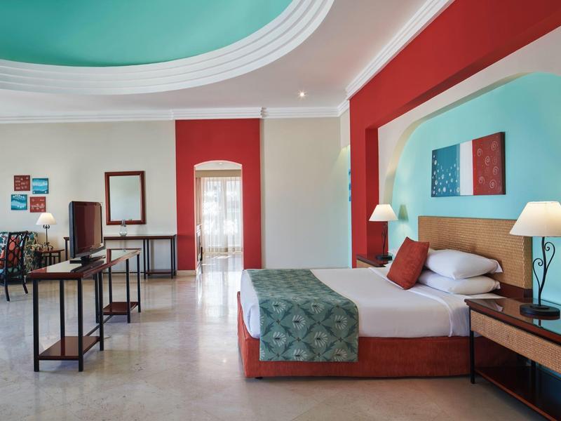 Chambre d'hôtel spacieuse avec lit double, décoration colorée et coin salon.