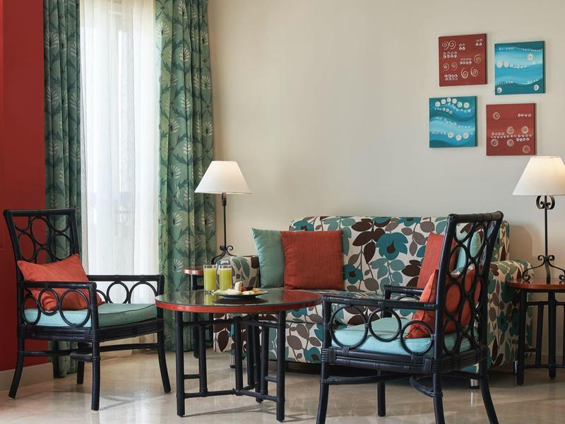 Espace salon d'hôtel confortable avec coussins colorés, fauteuils, canapé, lampes et décoration murale.