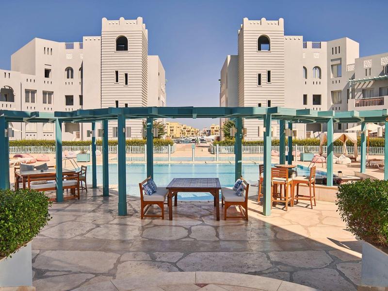 Espace extérieur avec tables et chaises à côté d'une grande piscine et bâtiments modernes beiges.