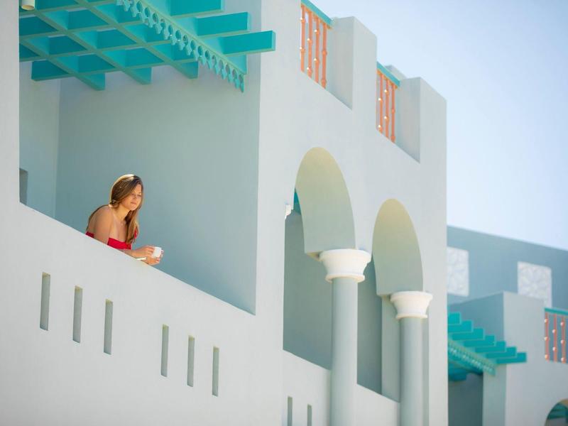 Deux personnes appuyées sur un balcon blanc avec des accents turquoise sous un ciel clair.