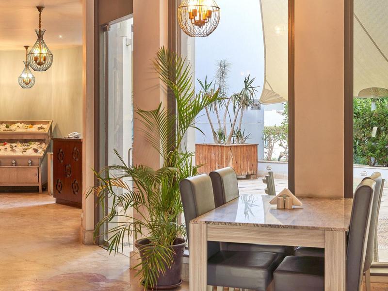 Espace repas d'hôtel confortable avec tables en bois, chaises, lumières suspendues et plantes d'intérieur.