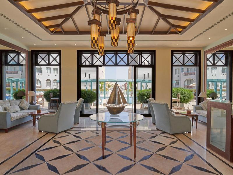 Grand hall d'hôtel avec canapés modernes, fauteuils, grandes fenêtres et éclairage décoratif.