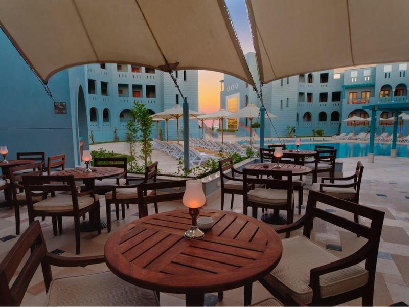 Espace de restauration en plein air près d'une piscine avec parasols et coucher de soleil.