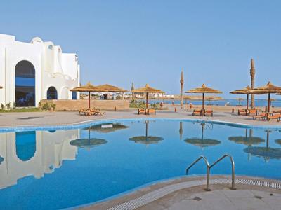 Piscina dell'hotel con ombrelloni e edifici bianchi sotto un cielo blu limpido.