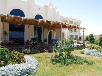 Hotelgebouw met natuurlijk rieten prieel en bloeiende tuin op de voorgrond.