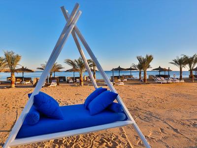 Blauw gevoerde schommelbank op zandstrand met palmbomen en parasols bij zee