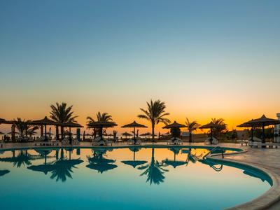 Rond hotelzwembad met palmbomen en ligstoelen bij zonsondergang.