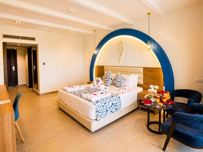 Chambre d'hôtel lumineuse avec lit double, arche bleue et coin salon avec canapé bleu et table.
