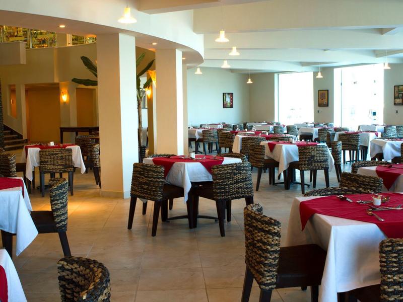 Sala da pranzo luminosa con tovaglie rosse e bianche e sedie intrecciate.