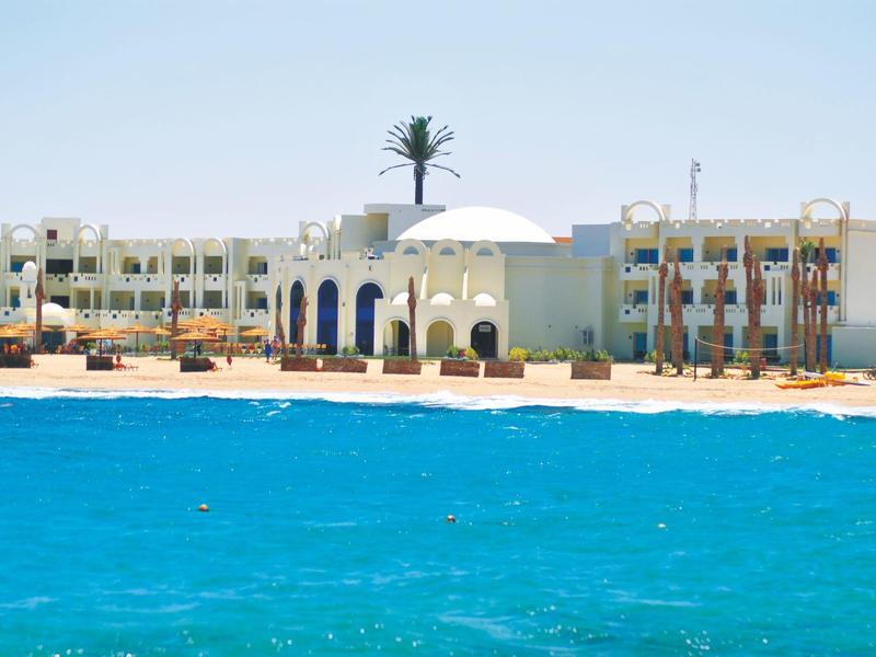 Hotel sulla spiaggia con acqua blu e architettura bianca sotto un cielo limpido.