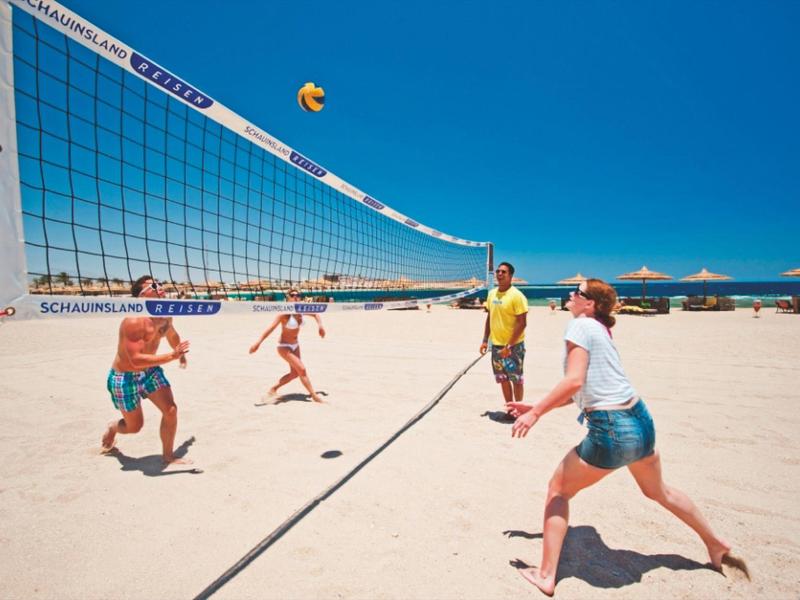 Quattro persone giocano a beach volley sulla sabbia di una spiaggia soleggiata.