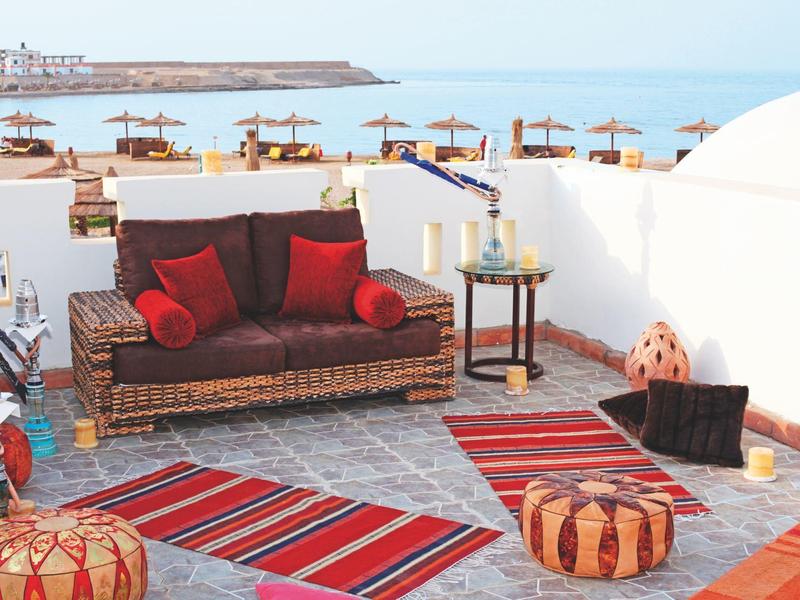 Terrazza con area salotto accogliente, tappeti colorati e vista sulla spiaggia e il mare.