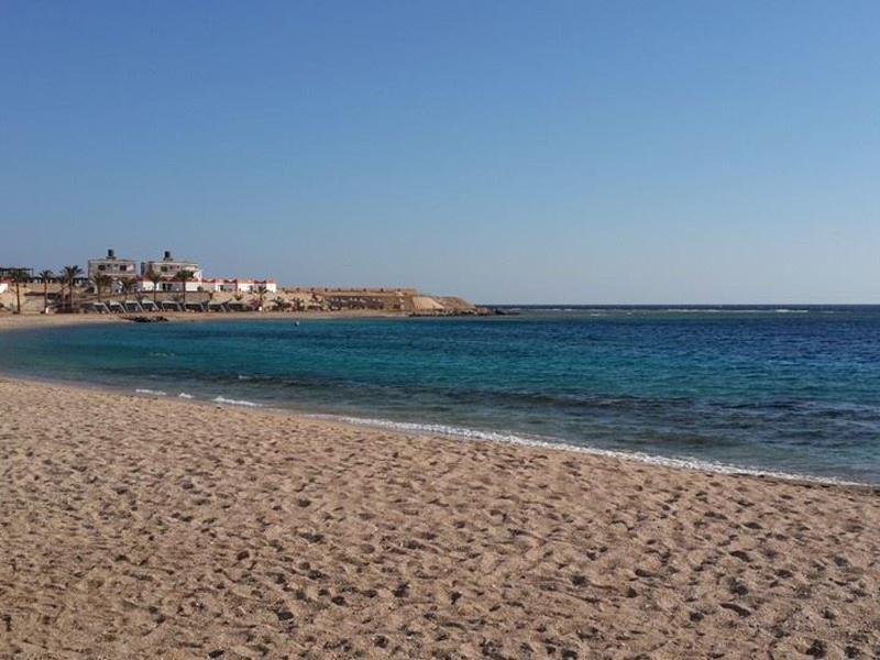 Ampia spiaggia di sabbia con mare blu calmo sotto un cielo limpido vicino a città costiera.