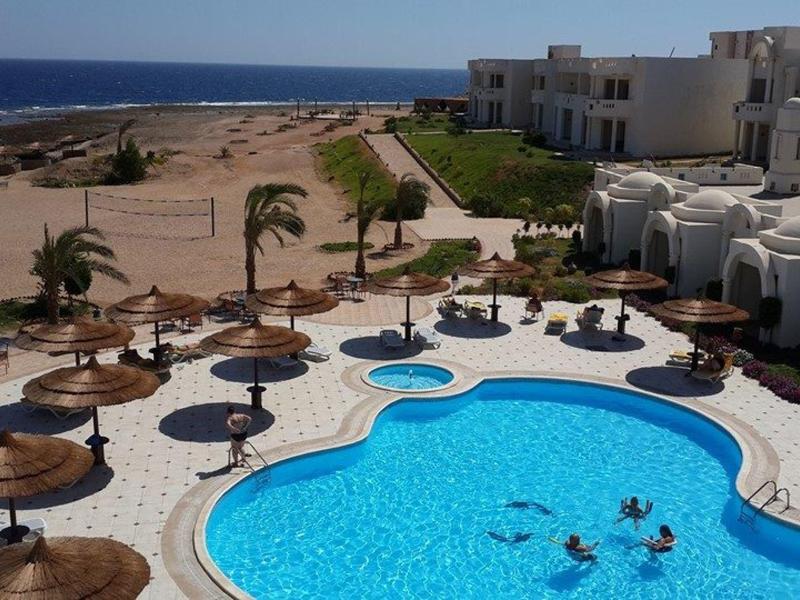 Grande piscina con ombrelloni rotondi e hotel adiacente sul mare.